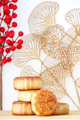 Vertical shot of delicious and sweet traditional Chinese Mid-Autumn Festival mooncakes on a wooden platter, with background patterned with autumn leaves and red Chinese hawthorn