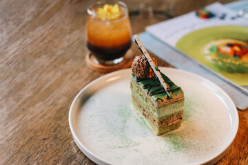 Green tea sliced cake dessert on white plate with summer mocktail in cafe table 