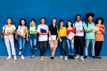 Group of multiracial teenage high school students looking at camera standing on blue background....