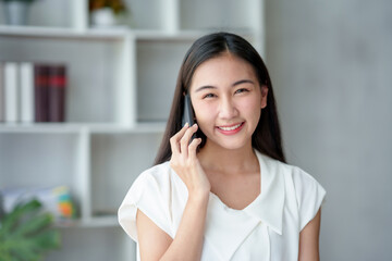 Fototapeta premium Young Asian businesswoman sit with her laptop computer happily talking on the phone with her customer explaining the detail in the office.