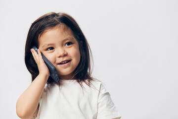 a little girl of preschool age, sitting on a white background in a white T-shirt, enthusiastically talking on the phone, turning half-side to the camera. The topic of the conversation on the phone