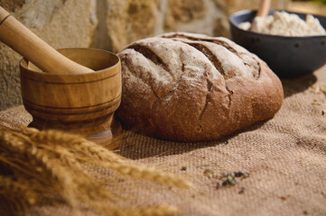 Still life. Traditional homemade wholesome sourdough wheaten bread, a wooden mortar and wheat spikelets on the sacklock