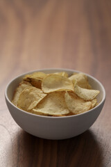 Organic potato chips with black pepper in white bowl on wood table