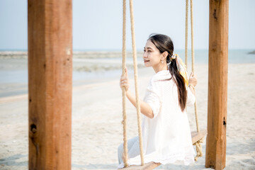 A girl sits on a swing and looks at the beautiful sea in the daytime on a rest day.