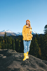 Naklejka premium Young woman with red hair full-length hiker in yellow raincoat and cap runs and walks on a mountain trip in the fall and hiking in the mountains at sunset freedom