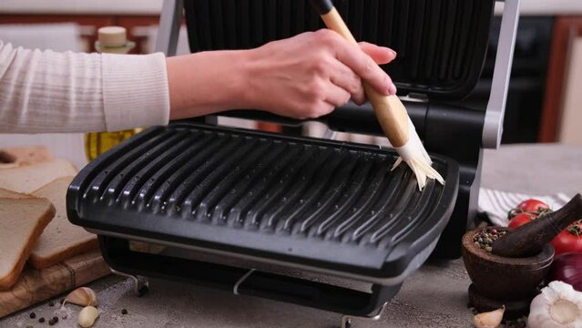 Woman greasing home electric grill surface with vegetable oil using brush