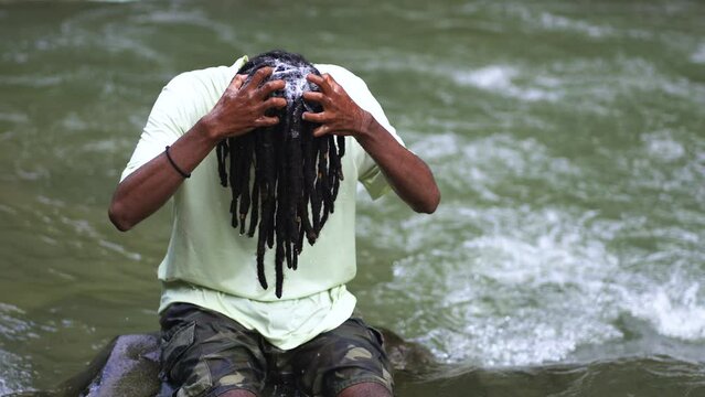 A Young Man With Dreadlocks Using Shampoo in the River