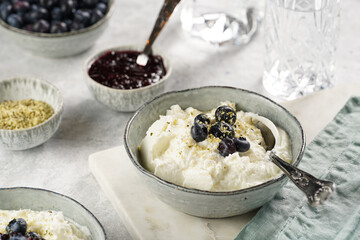 Two grey bowls with plain white icelandic diary breakfast skyr with jam, fresh blueberries, hemp seeds on marble board on grey background
