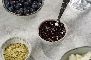 bowls with plain white icelandic diary breakfast skyr with jam, fresh blueberries, hemp seeds on marble board on grey background