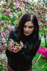 Fototapeta premium Young beautiful woman is holding blooming pink apple tree flowers in hands in rainy weather