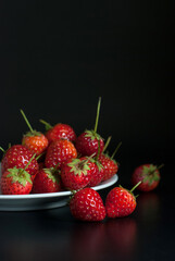 Several strawberries were on a white ceramic plate and placed on a black background.