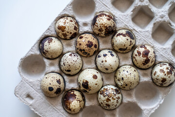 Spotted quail eggs in an egg box on a light background, natural eco-friendly products.