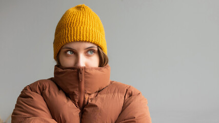 A woman in a warm jacket and hat sits on the bed at home and tries to keep warm. Home heating shutdown concept. Gas shutdown. - obrazy, fototapety, plakaty