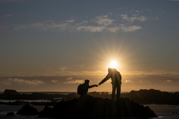 Hiker giving his hands helping partner climb up the rocks at sunrise.