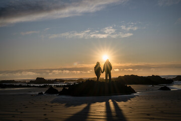 Couple holding hands, watching the sunrise at a rocky beach.  Catlins, South Island.