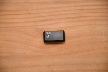 木目のテーブルの上に置かれたシフトキーのキートップ１つ