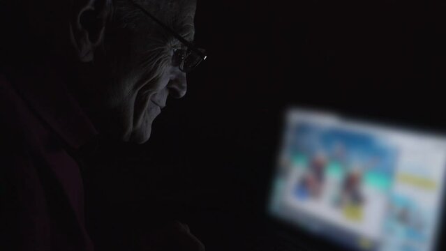 Smiling grandfather wearing glasses watching to laptop screen and looking at summer photo and image for vacation planning
