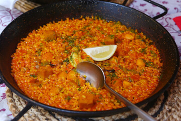 spanish paella close up photo in frying pan with shrimps, peas and lemon slice