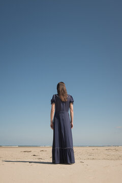 rear view of woman in classic blue dress standing on the beach 