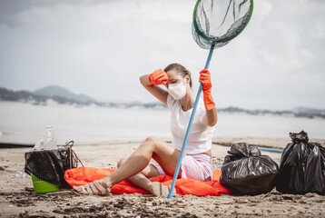 A female ecologist volunteer is resting after cleaning the beach on the seashore from plastic and other waste