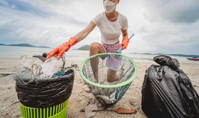A female ecologist volunteer cleans the beach on the seashore from plastic and other waste