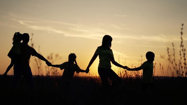 Happy family silhouette at sunset. Group of people friends in field. Parents and children walk in meadow in grass. Girls and boys walk together in park at sunset. Family fun in summer at picnic.