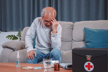 Asian senior elderly mature man feel stress headache sitting on sofa in living room. Old man touching his temples from horrible migraine. Health care and medical insurance concept.