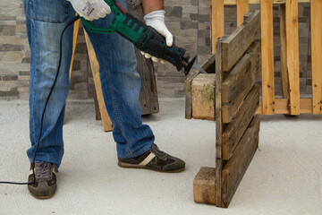 Image of the hands of a construction worker who cuts pallets of pallets with a hacksaw. Do-it-yourself and construction work. Cutting of wood planks
