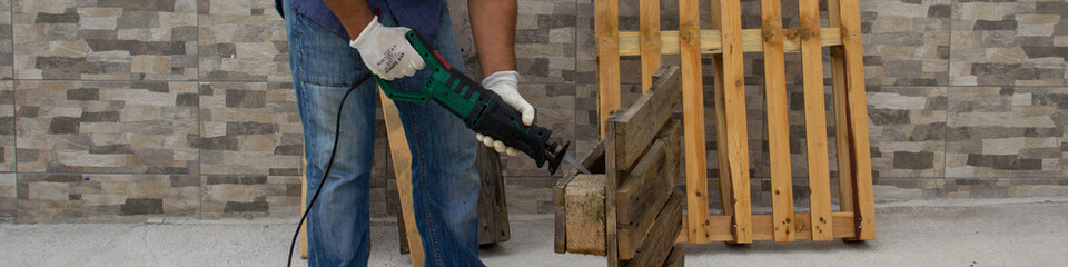 Image of the hands of a construction worker who cuts pallets of pallets with a hacksaw. Do-it-yourself and construction work. Cutting of wood planks. Horizontal banner 
