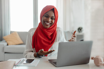 Cheerful black muslim woman in hijab having video chat with friends or online meeting, talking to...