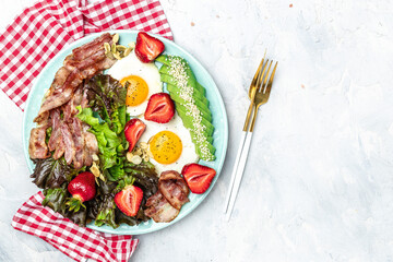 Fried egg bacon with avocado, strawberries and fresh salad. Delicious breakfast or lunch, Ketogenic, keto or paleo diet, Food recipe background. Close up