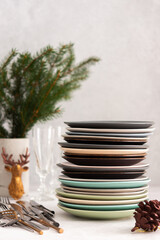 Preparing for a festive table setting, a stack of different plates and forks with knives, fir branches in a concrete vase, Christmas decorations