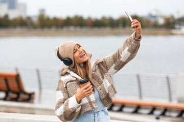 Photo of a young happy woman taking a selfie with her smartphone during outdoor walk.