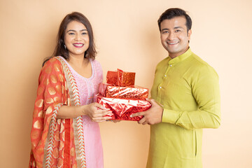 Happy young indian couple holding gift box celebrating diwali festival together isolated on studio...