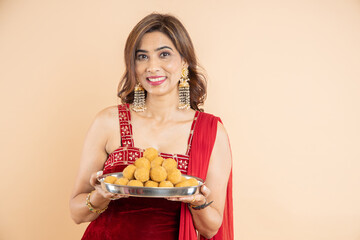 Portrait of beautiful indian woman holding plate full of laddu or laddoo sweets celebrating diwali...