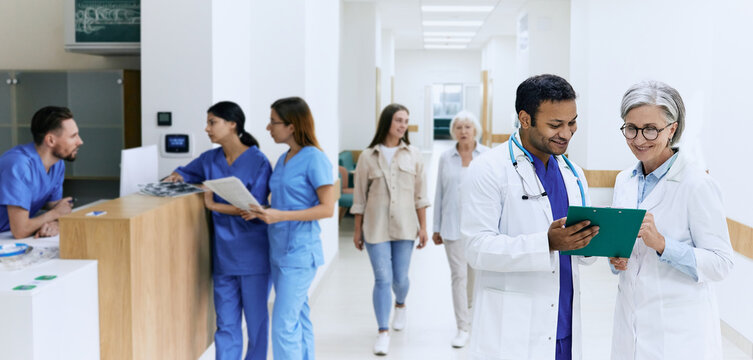 Working Day In Medical Clinic, View Of Lobby With Doctors In White Coats, Nurses, Assistants And Walking Along Hospital Corridor Patients