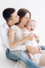 Happy family with baby boy sits, embraces and kisses each other.