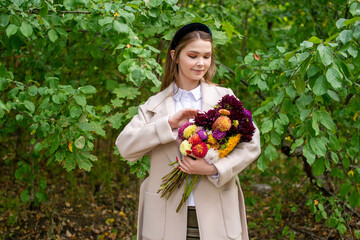 A cute girl with a black headband and long hair holds a bouquet of autumn flowers and corrects it