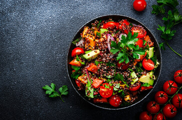Quinoa tabbouleh salad with tomatoes, paprika, avocado, cucumbers, onion and parsley. Traditional Middle Eastern and Arabic dish. Black kitchen table background, top view