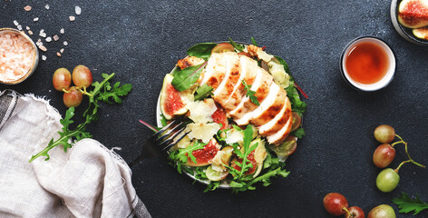 Grilled chicken fillet with fig, grape, arugula and chard salad. Black table background, top view banner