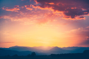 Spectacular sunrise over mountain range under mist in the morning light. Colorful clouds in orange...