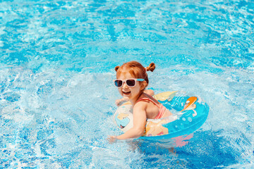 Cute toddler girl wear sunglasses having fun in swimming pool with blue clean water. Family...
