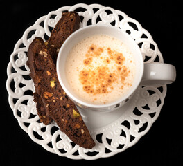 Chocolate biscotti with a white mug of cappuccino on white plate, on black background. Image from...