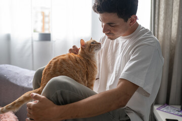 close up. young man interacts with a brown tabby cat by the window