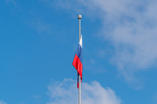 Tricolor flag of Russia white blue red on a flagpole against a blue sky and white clouds closeup.