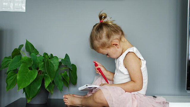 Little girl draw or write by red pencil at home. Child creativity and education concept