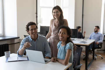 Happy business coworkers at laptop, diverse office employees at shared workplace corporate portrait. Successful multiethnic team working on project together, looking at camera, smiling, laughing
