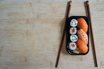 Japanese fast food, delicious sushi in a black plastic box on a bamboo wooden board with chopsticks.