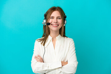 Telemarketer English woman working with a headset isolated on blue background keeping the arms...