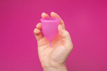 menstrual cup in female hand on pink background, feminine hygiene product
